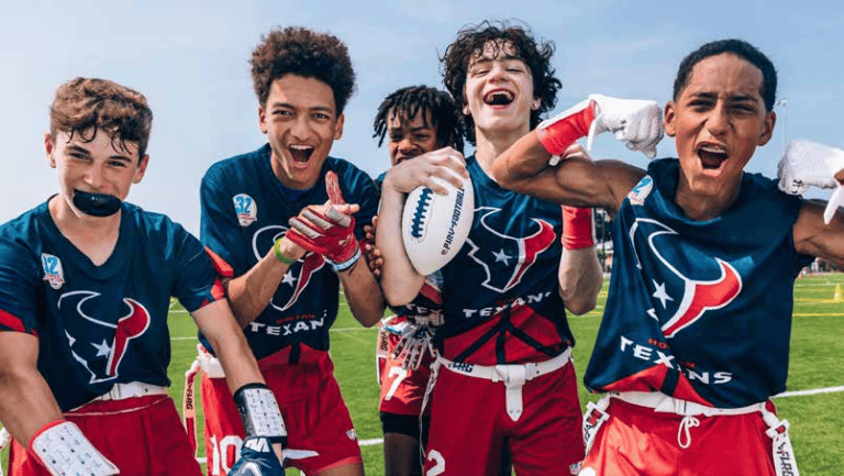 Three students in NFL FLAG uniforms celebrate together on the field, one holding a football
